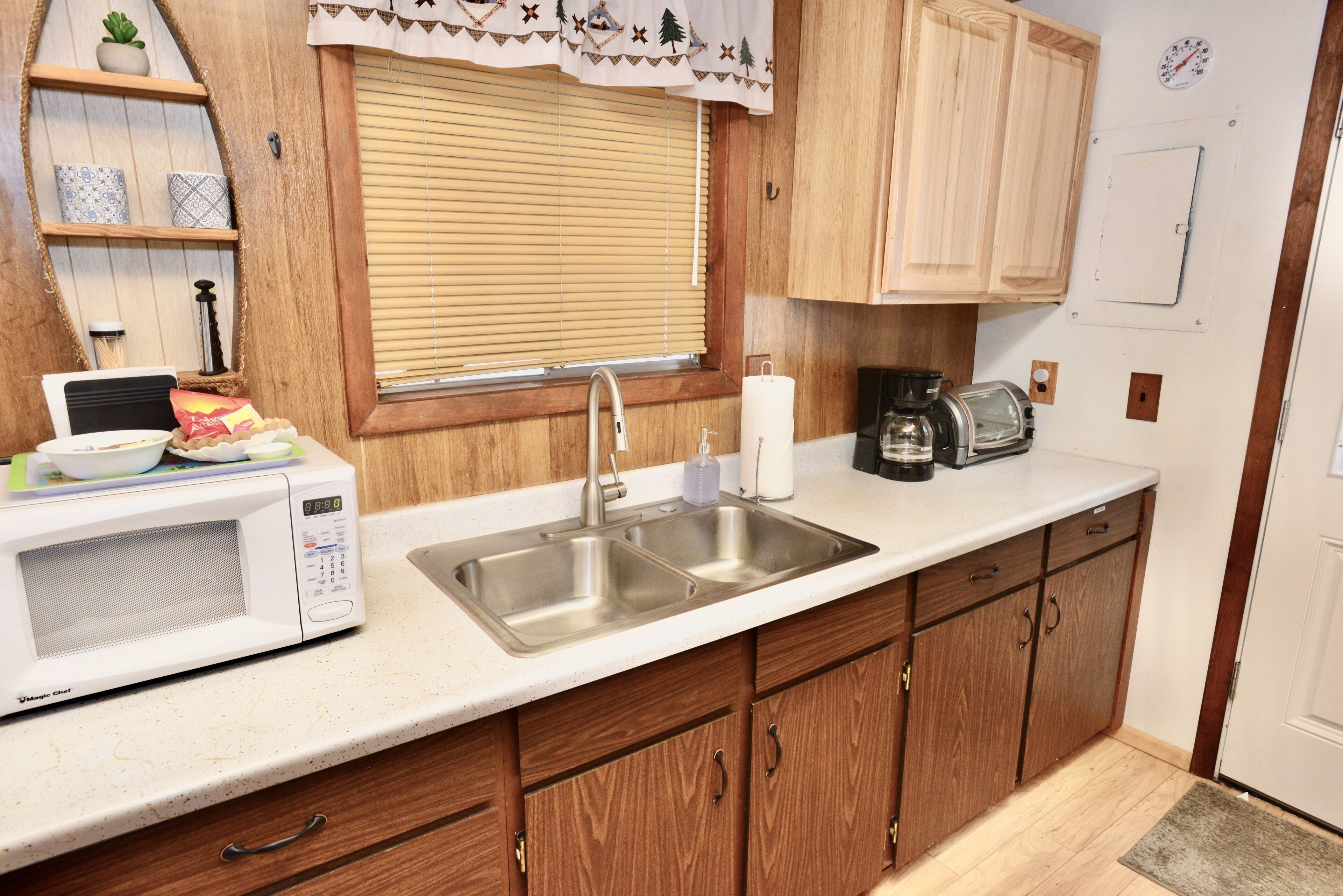 A kitchen with wooden cabinets, a white countertop, a microwave, a sink, and a window with blinds.