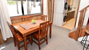 A wooden dining table with chairs, a small plant, and a view of a kitchen with a washing machine. - Mint Chip Cabin - Pet friendly - Forested - Large deck - Fire pit (Cascade)