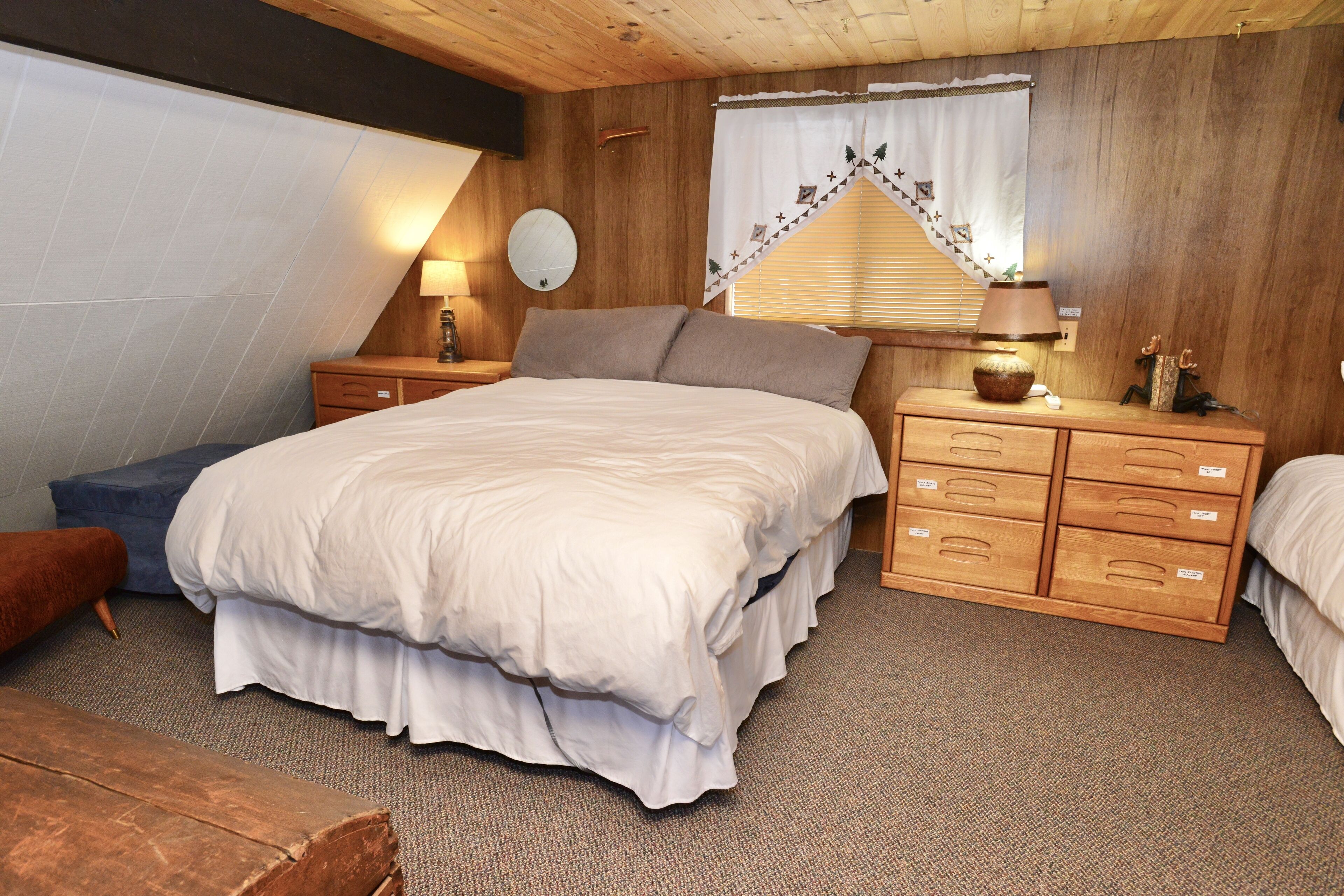 Ein Schlafzimmer mit einem großen Bett, Nachttischen aus Holz, einer Kommode und einem Fenster mit Vorhängen.