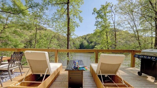 A wooden deck with two cushioned chairs and a small table, surrounded by trees. - Lakefront Home w/ Dock · King Suite · Stunning Paradise · Voted Best of Kentucky (Laurel County)