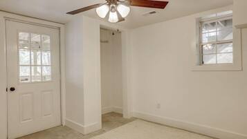 A room with a white door, a ceiling fan, a window, and a door leading to a hallway.