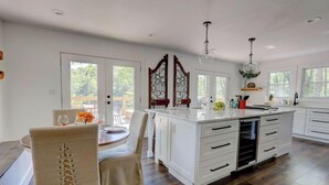 A spacious kitchen with white cabinetry, a central island, and a dining area with a round table and chairs. - Lakefront Home w/ Dock · King Suite · Stunning Paradise · Voted Best of Kentucky (Laurel County)