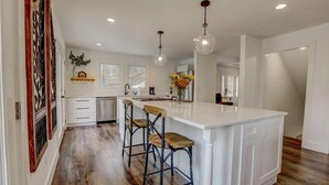 A modern kitchen with a large island, bar stools, pendant lights, and a wooden floor. - Lakefront Home w/ Dock · King Suite · Stunning Paradise · Voted Best of Kentucky (Laurel County)