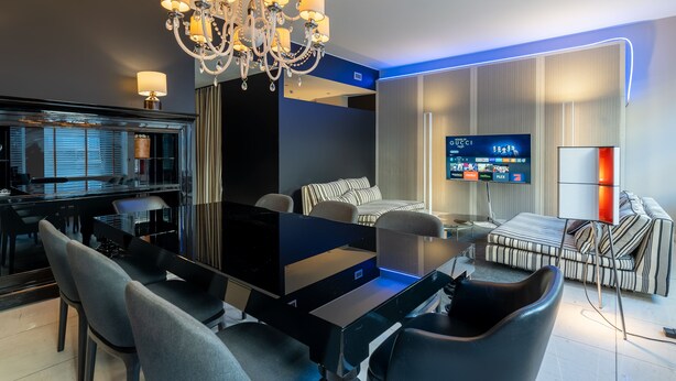 A modern hotel room with a dining area, a large TV, a chandelier, and a sofa. - The King Of Milan (Milan)