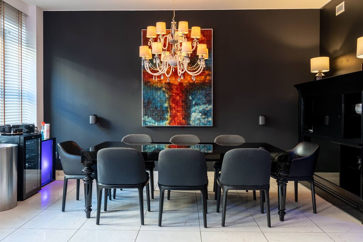 A modern dining area with a black wall, a chandelier, and a colorful abstract painting.