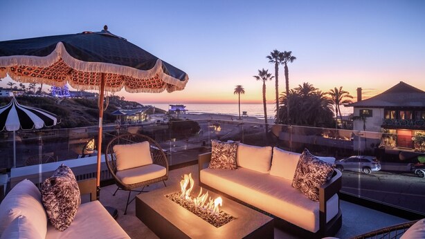 Une terrasse sur le toit avec un foyer, des sièges d’extérieur et une vue sur la plage et l’océan au coucher du soleil.