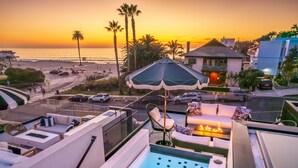 Une terrasse sur le toit avec une piscine, des chaises longues et une vue sur le coucher de soleil au-dessus de la plage.