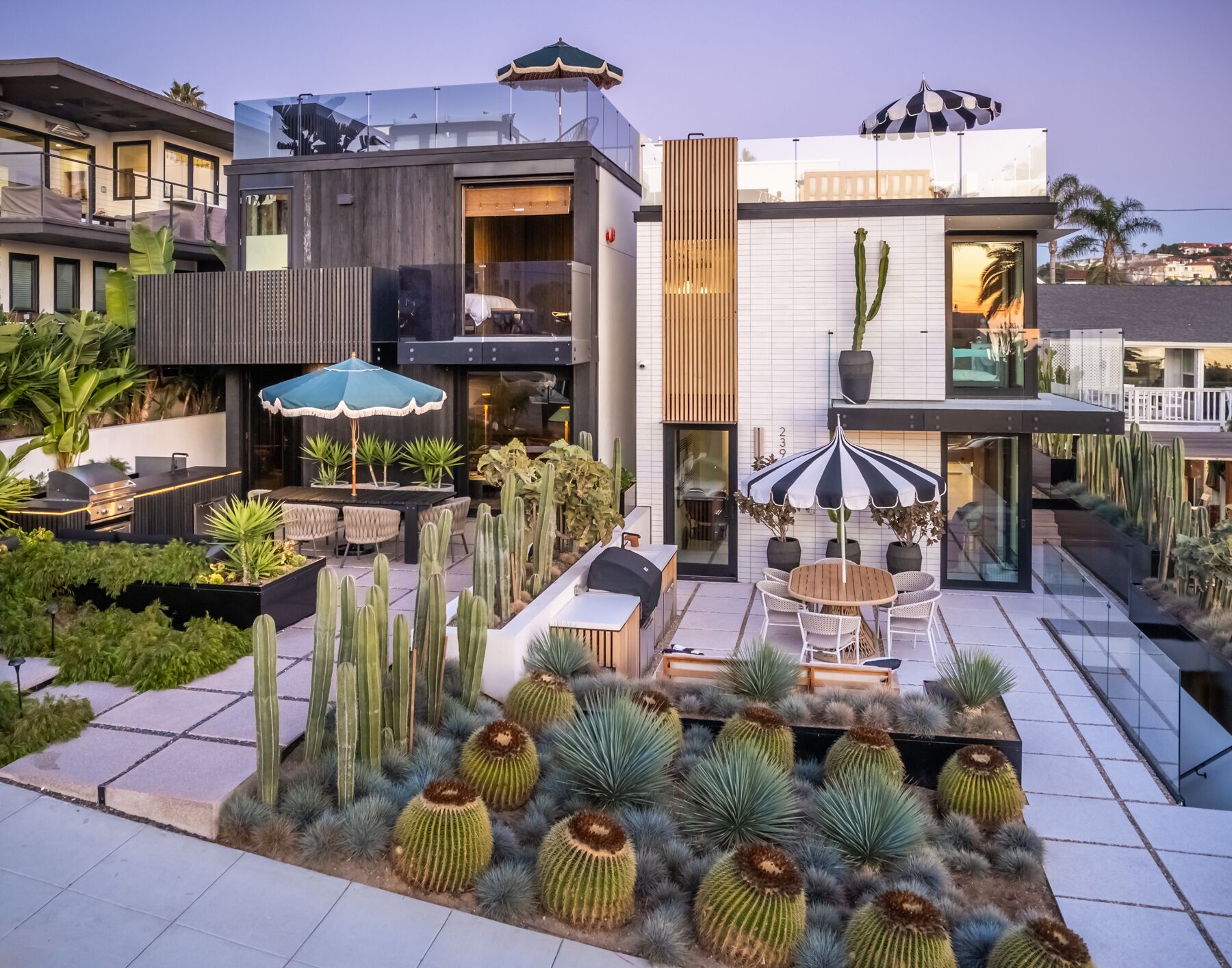 A modern outdoor patio area with a dining set, multiple umbrellas, and a variety of cacti.