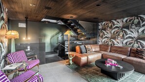 Un salon moderne avec un canapé en cuir, des fauteuils à rayures, une table basse et un escalier menant à un niveau supérieur.