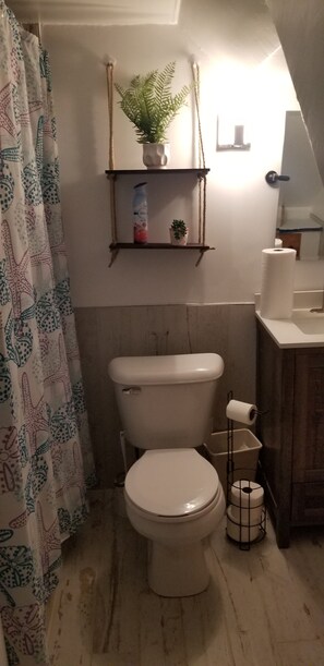 A bathroom with a toilet, a shelf with a plant, a roll of toilet paper, and a shower curtain with a starfish pattern. - Toledo, lakeside home 3 bdrm sleep 7 on Lake Erie with 4 decks
to choose from. (Toledo)