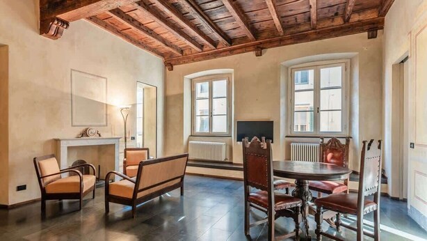 A dining area with a round table and chairs, a fireplace, and large windows with shutters. - Appartamento della Zecca - Affitti Brevi Italia (Lucca)