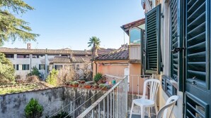 A balcony with white chairs, a small table, and a view of neighboring buildings. - Appartamento della Zecca - Affitti Brevi Italia (Lucca)