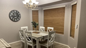 A dining area with a round table, white chairs, a wall clock, and a chandelier. - River house with scenic view (Bullhead City)