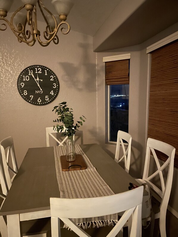 A dining room with a wooden table, white chairs, a clock, and a window with blinds. - River house with scenic view (Bullhead City)