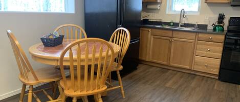 A kitchen with wooden cabinets, a black refrigerator, a dining table with chairs, and a window with blinds.