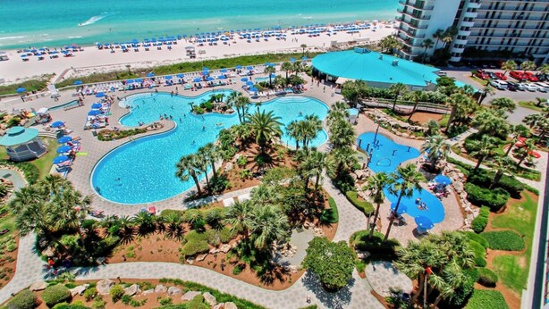 Een resort met meerdere zwembaden, een strand en een hotelgebouw.