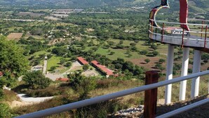 Un belvédère offrant une vue panoramique, doté d’une rambarde en métal, d’une structure rouge et blanche, et donnant sur une vallée parsemée de bâtiments et de verdure.