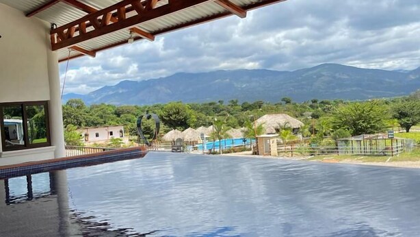 Une piscine intérieure avec vue sur les montagnes et, en arrière-plan, une structure dotée d’un toit de chaume.