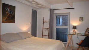 Ein Schlafzimmer mit Bett, Schreibtisch, Stuhl, einer Leiter, einem Fenster und einem Gemälde an der Wand.