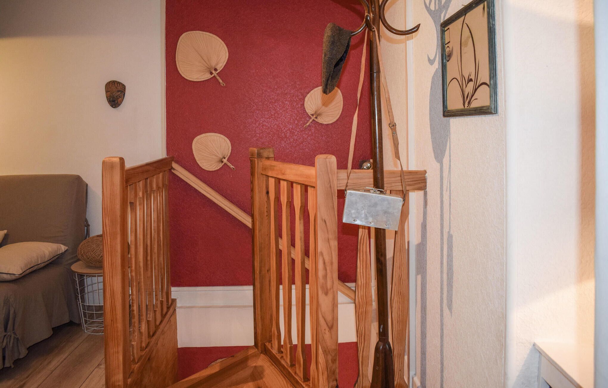 Una scala di legno con una parete rossa e una porta bianca. Si vedono tre ventilatori appesi al muro.