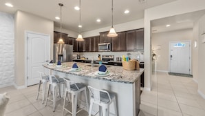 A modern kitchen with dark cabinets, a large island with bar stools, stainless steel appliances, and pendant lighting.