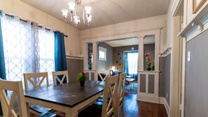 A dining area with a wooden table and chairs, a chandelier, and a view into another room.