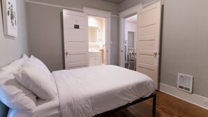 A bedroom with a bed, white walls, wooden flooring, and white doors leading to other rooms.