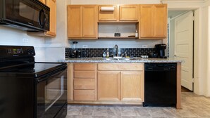 A modern kitchen with wooden cabinets, a black microwave, a dishwasher, and a granite countertop.
