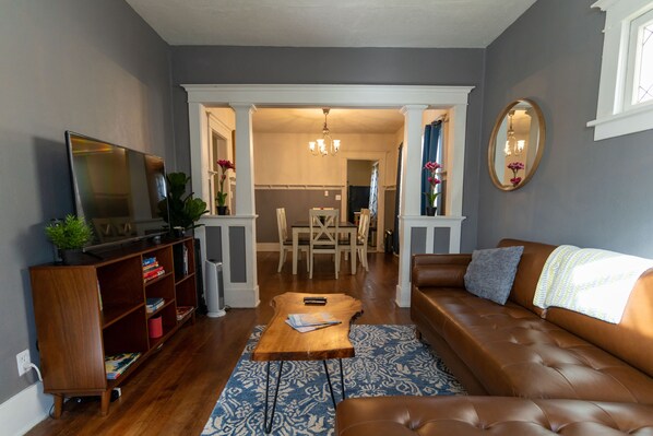 A living room with a brown leather sofa, a wooden coffee table, a bookshelf, and a television. - Charming Central Tacoma Home Located Near 6th Ave (Tacoma)