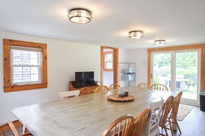 Un comedor con una mesa de madera, sillas, un televisor y vistas al exterior.