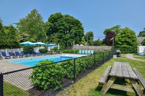 Un patio trasero con piscina, sillas de descanso y una mesa de picnic.