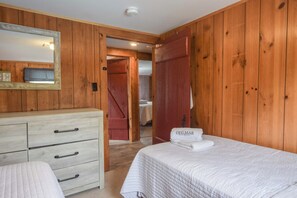 Habitación con paneles de madera, una cama, un aparador y un baño visible a través de una puerta abierta.