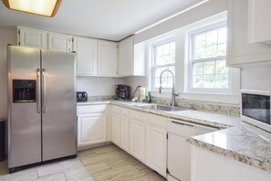Una cocina moderna con armarios blancos, un refrigerador de acero inoxidable, un lavavajillas integrado, una encimera de granito y una ventana que proporciona luz natural.