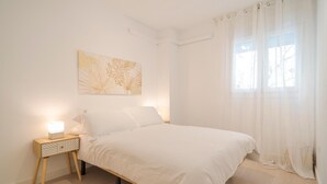 Un dormitorio con cama, mesita de noche y ventana con cortinas.
