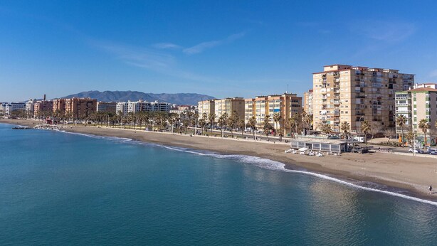 Un paisaje urbano costero con una playa, edificios altos y palmeras.