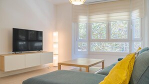 Una sala de estar moderna con un televisor de pantalla plana sobre un mueble de madera, una mesita de madera y un sofá gris con cojines amarillos.