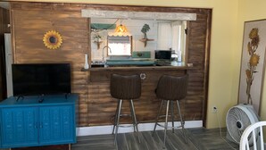 A kitchen area with a wooden counter, two bar stools, a sink, a microwave, and a TV on a blue cabinet. - Nature Coast Inn and Cottages (Inglis)