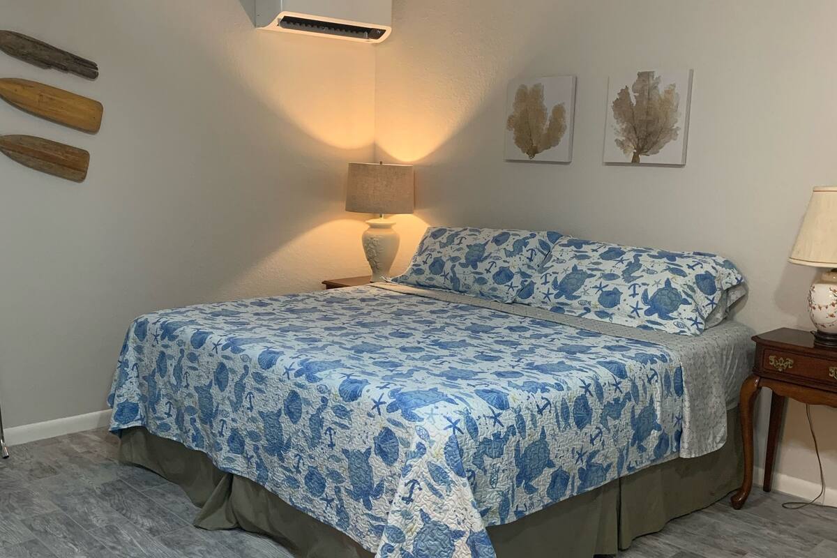 A bedroom with a bed, a nightstand, a lamp, and wall-mounted artwork.