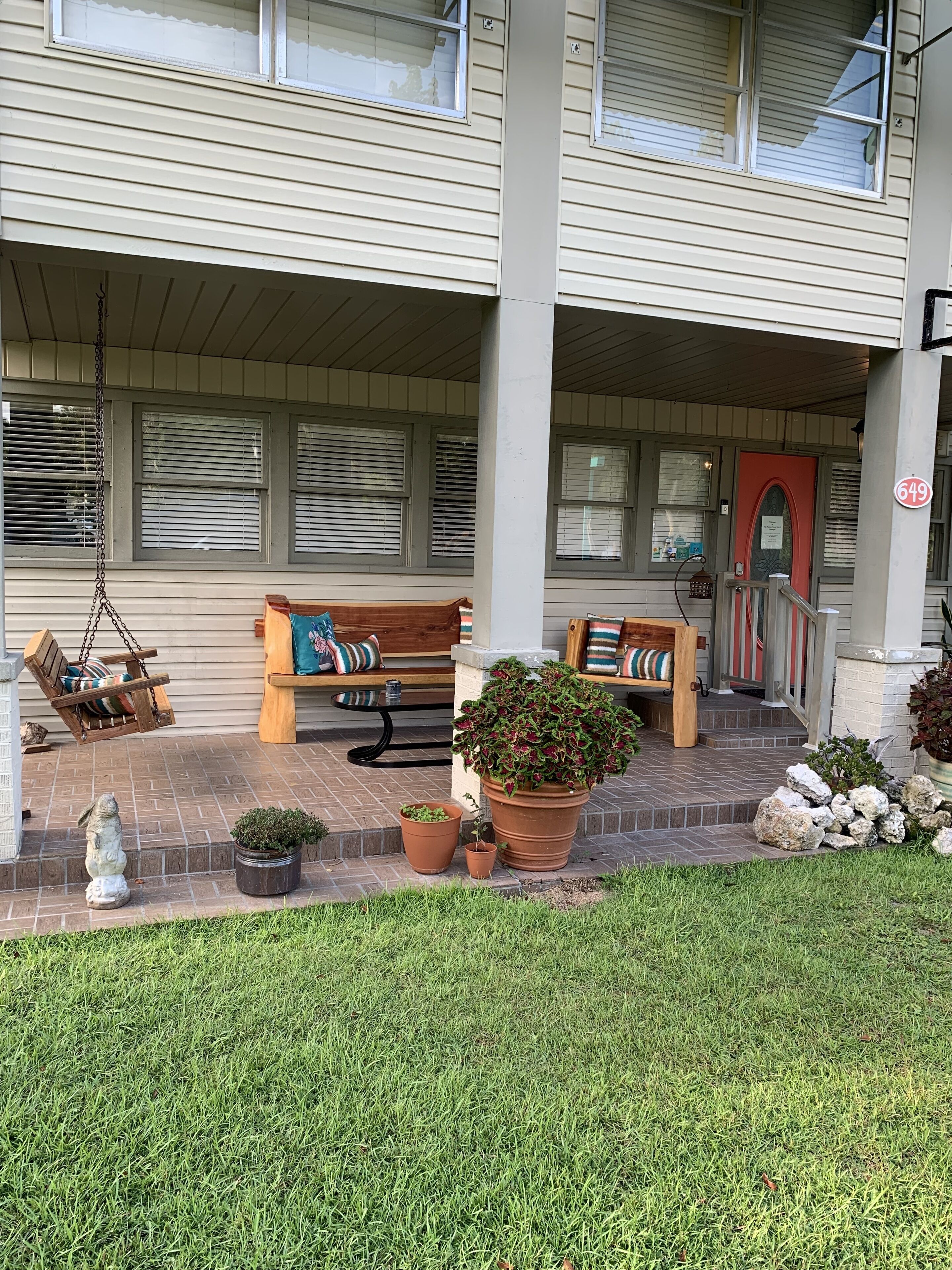 A covered porch with a bench, a hanging swing, and potted plants.