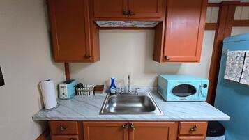 A compact kitchen with wooden cabinets, a sink, a toaster, a microwave, and a blue appliance.
