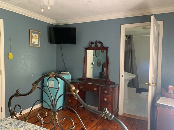 A bedroom with a wooden dresser, a bed with ornate metal headboard, a flat-screen TV mounted on the wall, and a bathroom visible through an open door. - Nature Coast Inn and Cottages (Inglis)