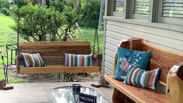 A wooden bench with cushions, a glass table with a 'WELCOME' sign, and a brick patio. - Nature Coast Inn and Cottages (Inglis)