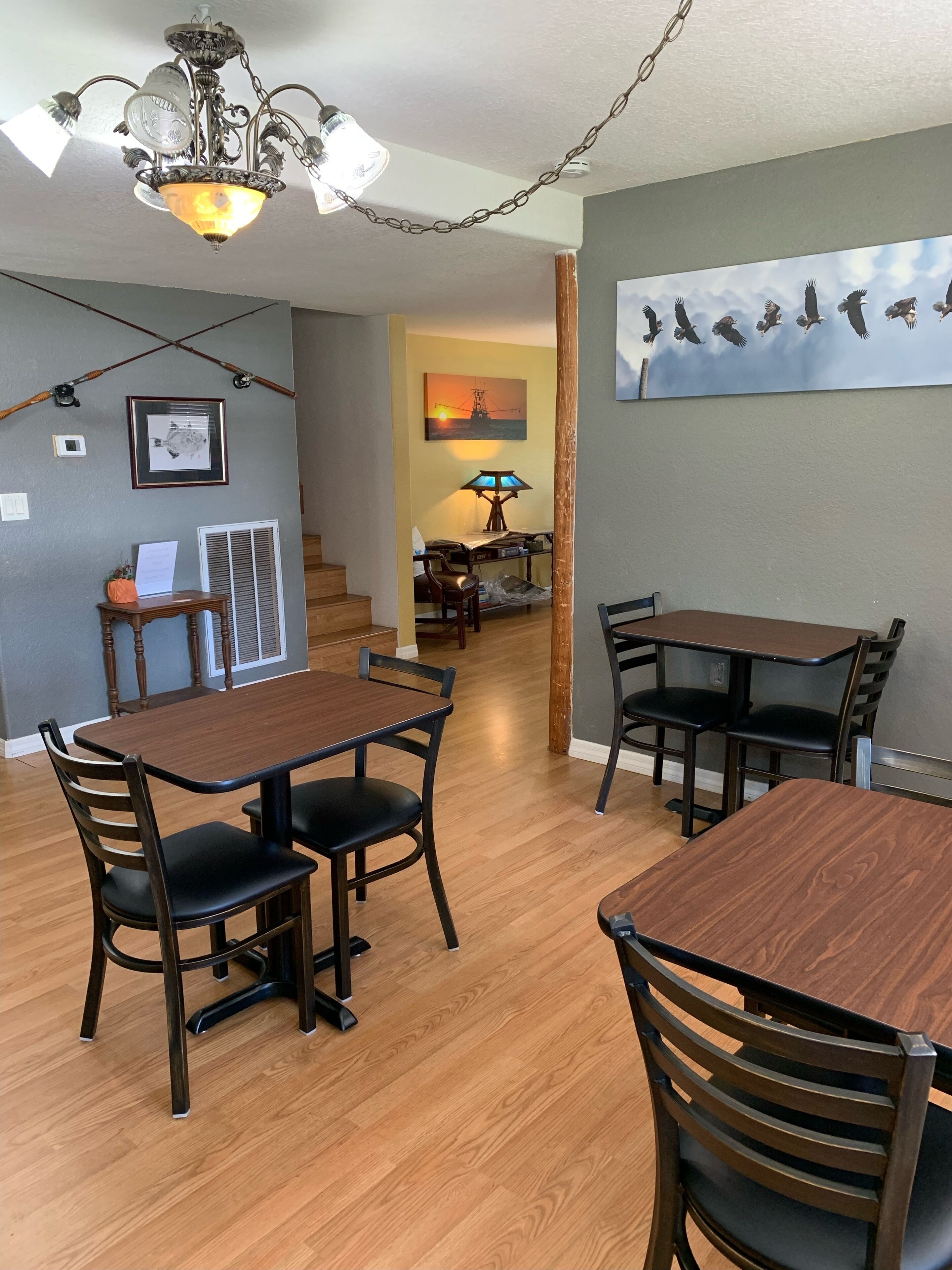 A dining area with wooden tables and chairs, a chandelier, and a painting of birds on the wall.