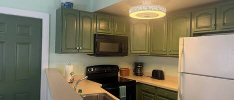 Una cocina con gabinetes verdes, microondas, estufa, fregadero y refrigerador.