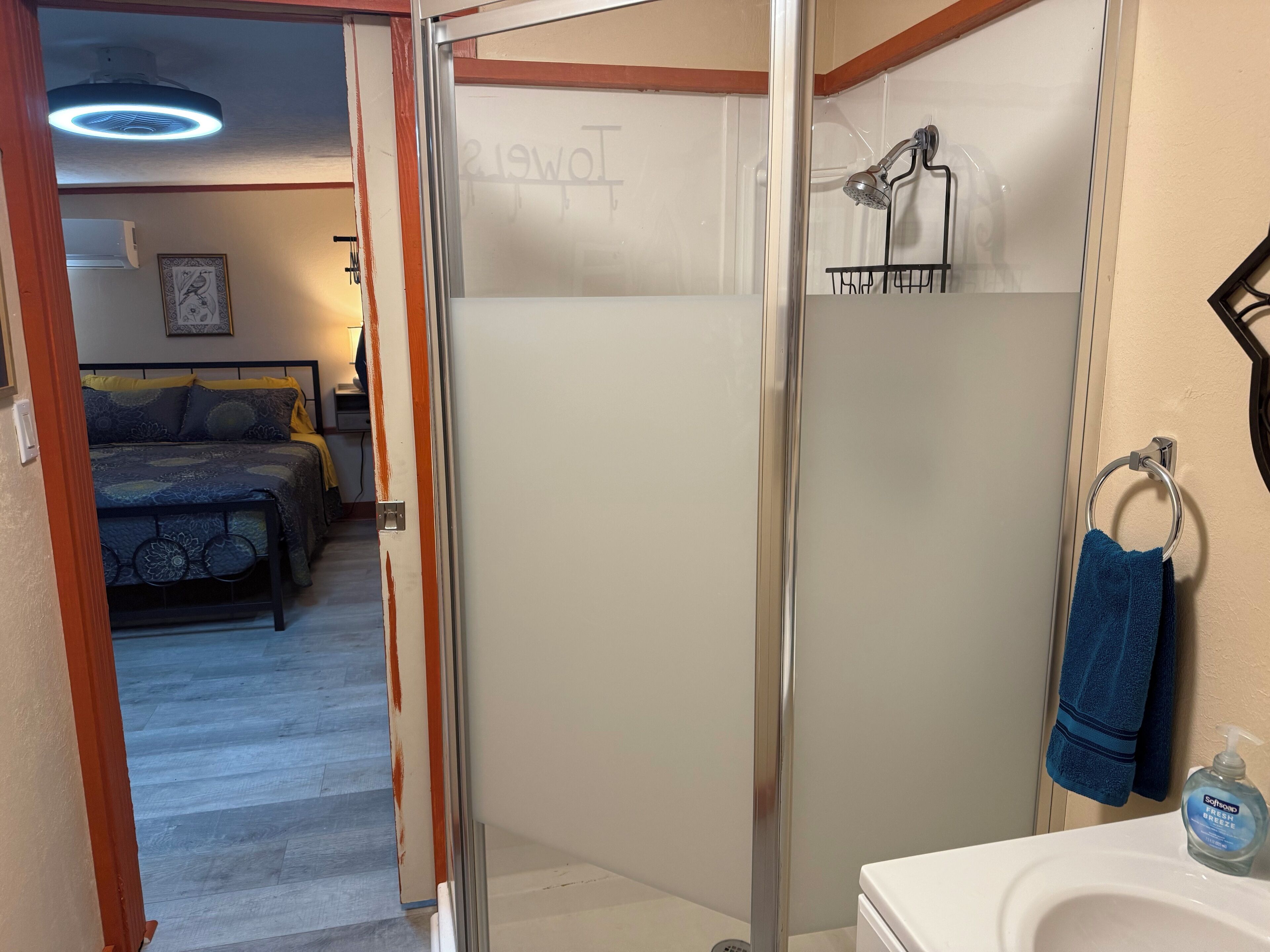 Une salle de bain d’hôtel avec une douche à parois de verre, un lavabo avec un distributeur de savon et un porte-serviettes avec une serviette bleue.