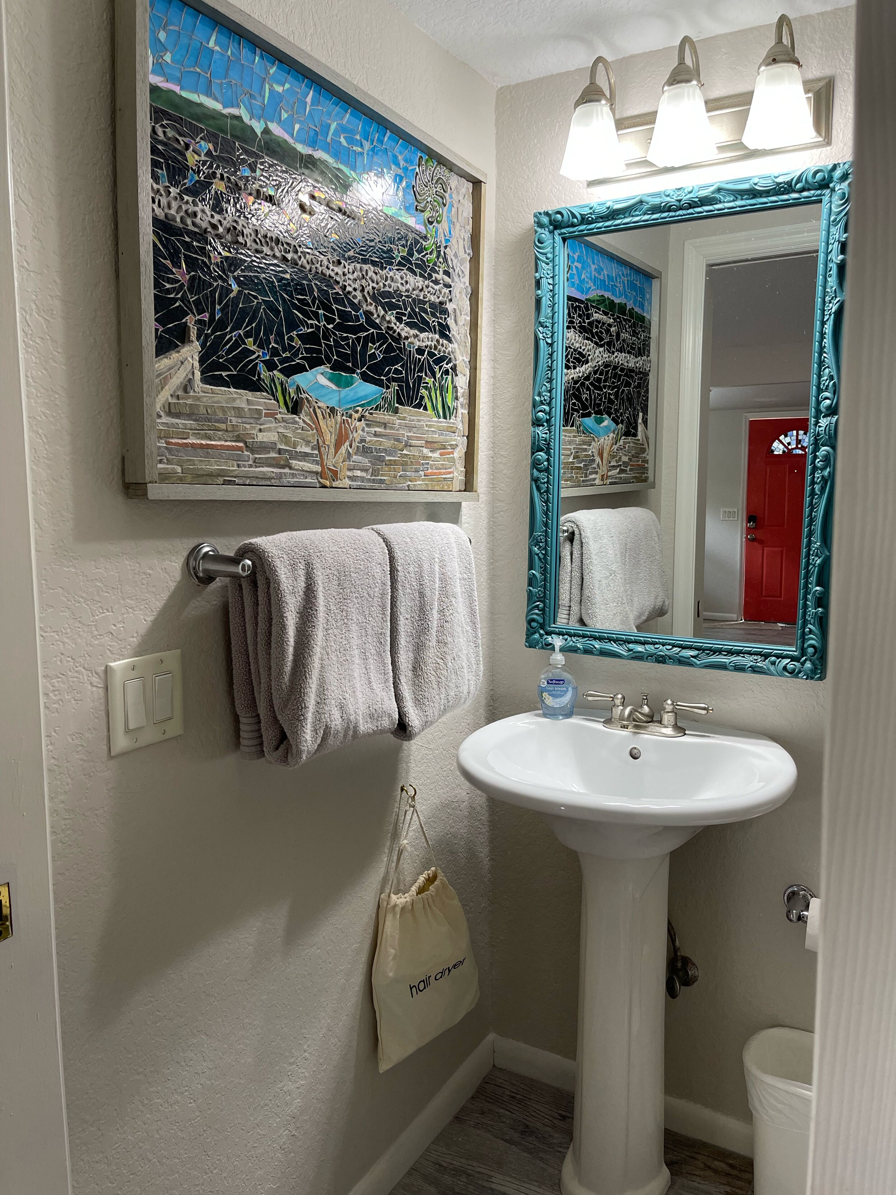 A bathroom with a white sink, a mirror with a teal frame, a towel rack with a towel, and a wall-mounted light fixture.