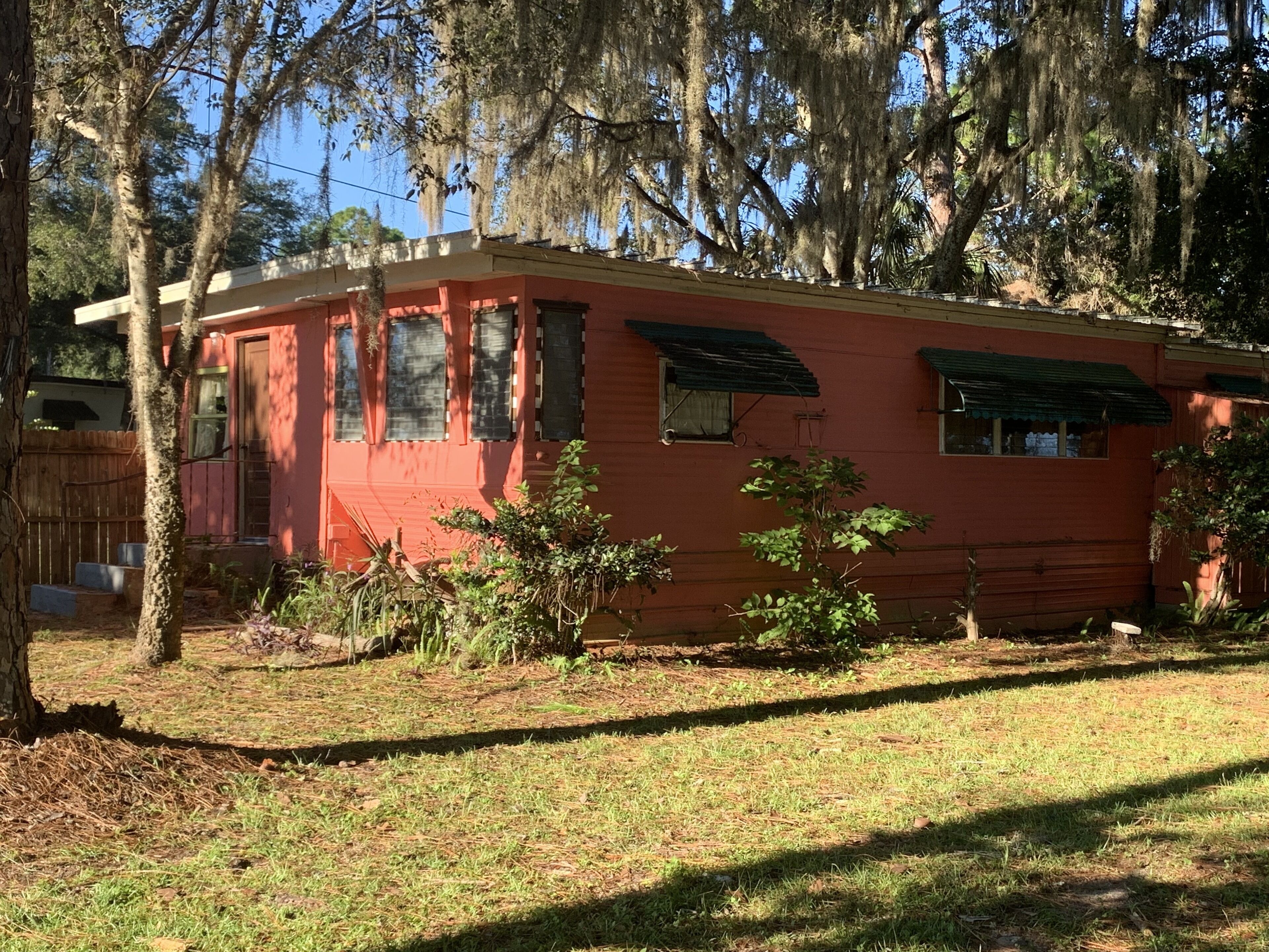 Una casa roja de un piso con porche delantero, rodeada de árboles y una valla de madera.