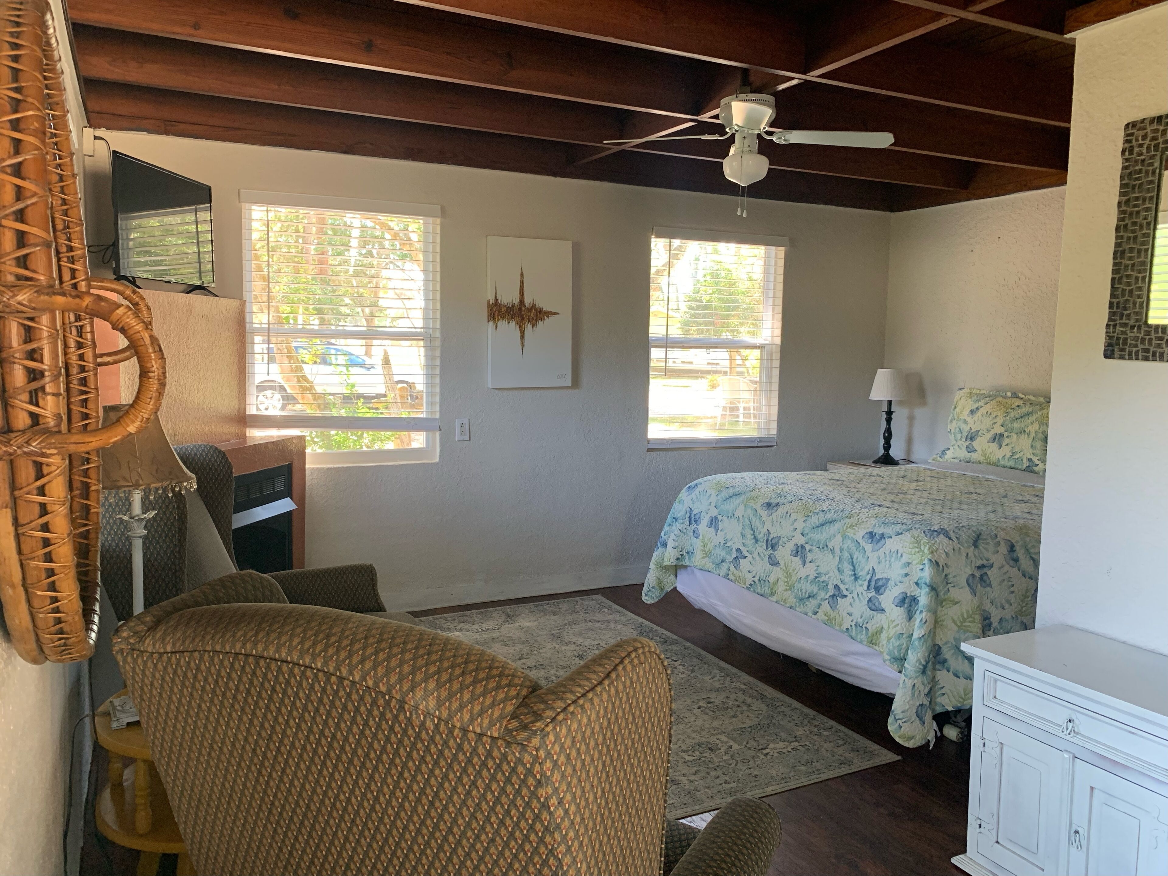 A bedroom with a bed, a desk, a chair, a ceiling fan, and two windows.