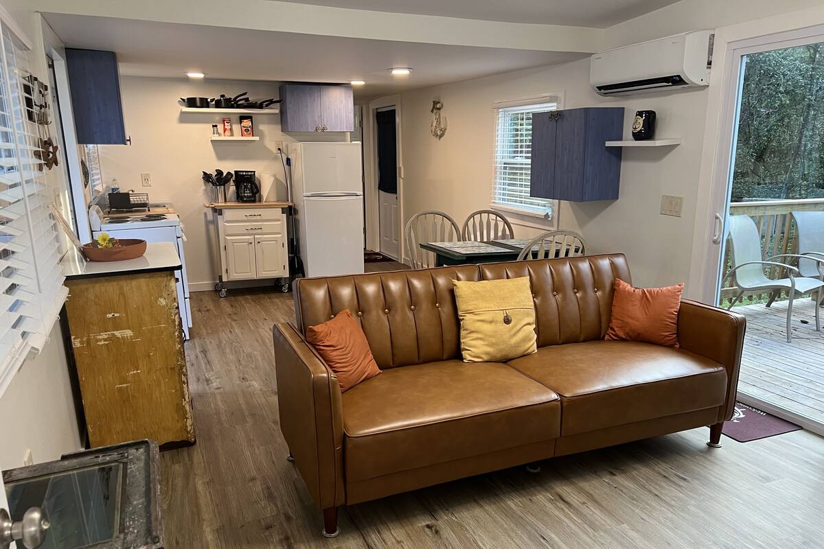 A cozy living room with a brown leather sofa, a dining area with a table and chairs, and a kitchen with a refrigerator and cabinets.