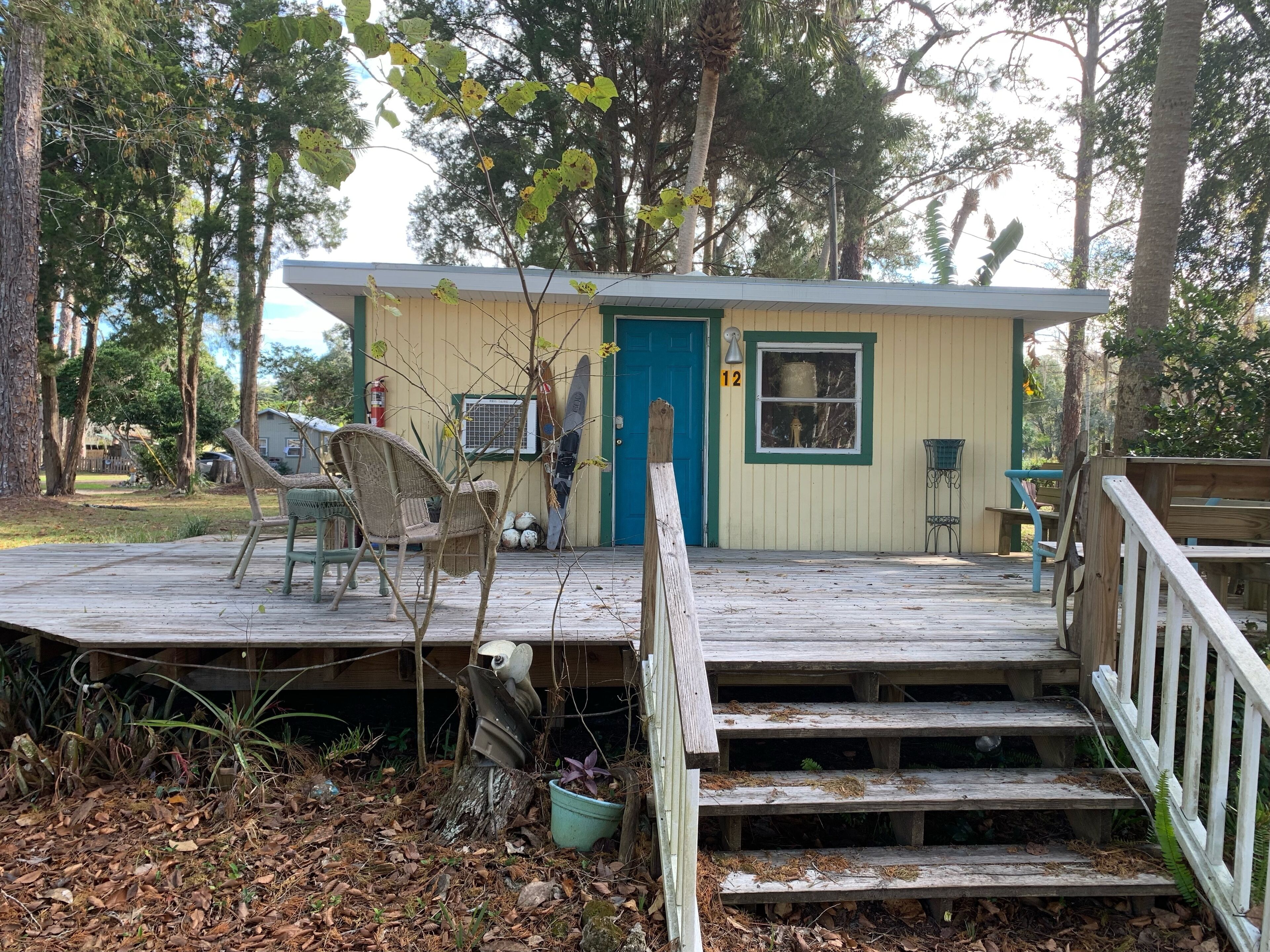A small wooden cabin with a deck, a blue door, and a number '12' sign.